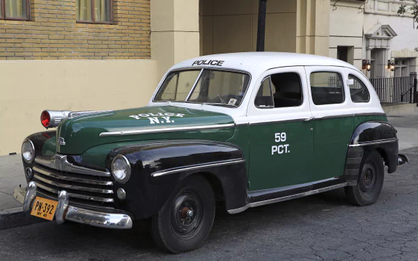 HD PC desktop wallpaper featuring a classic Ford police vehicle in green, black, and white parked on a city street, showcasing vintage law enforcement design.