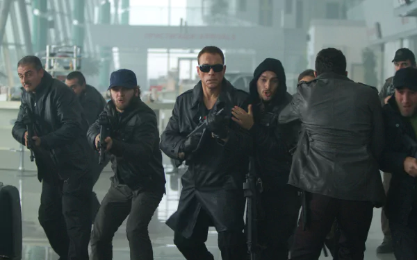 A high-definition wallpaper featuring Jean-Claude Van Damme as Vilain in The Expendables 2, surrounded by armed characters in an intense action scene.