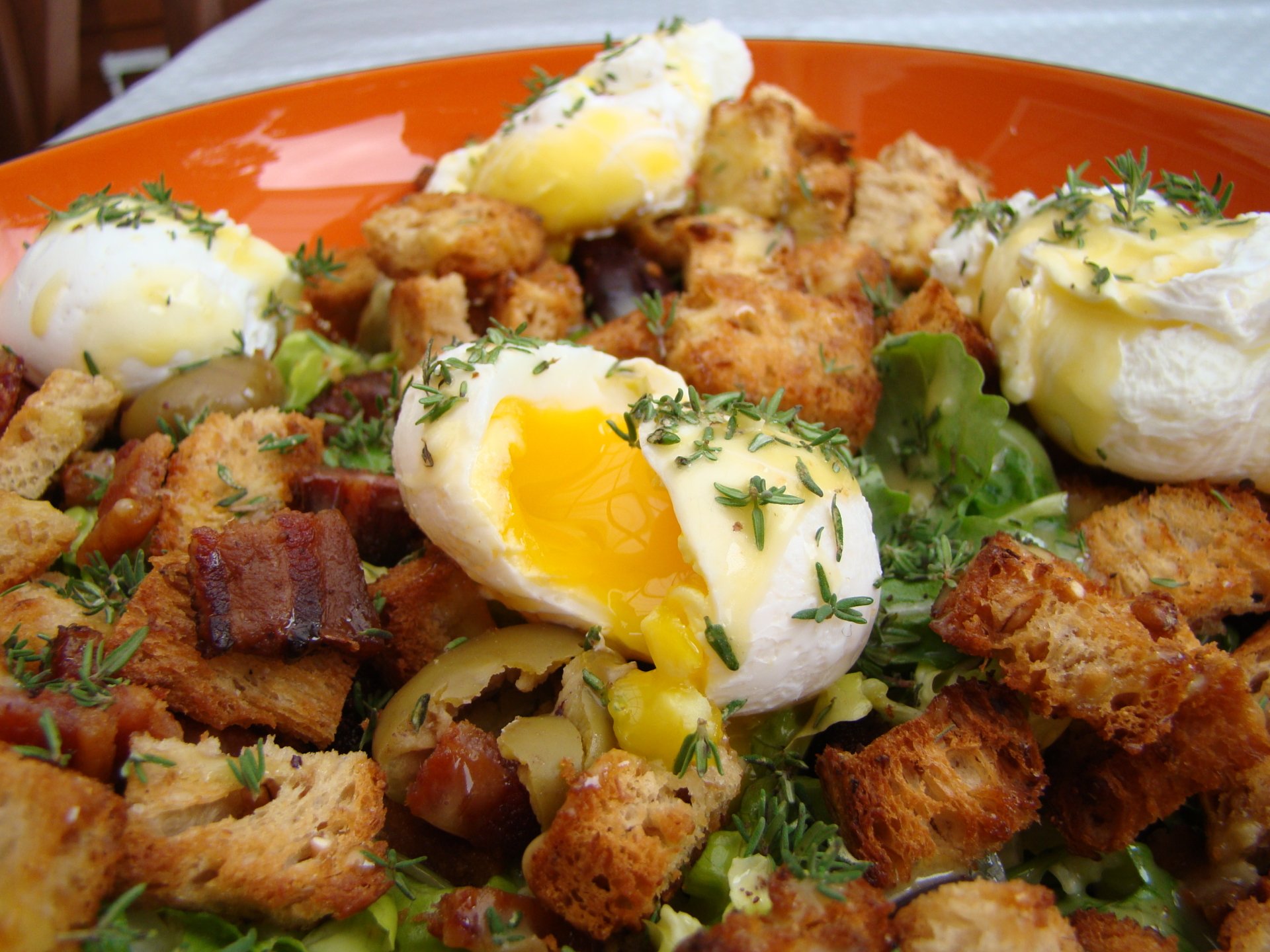 Close-up of a Salade Lyonnaise featuring poached eggs, crispy bacon, croutons, and greens, captured in HD as a vibrant lunch meal desktop wallpaper.