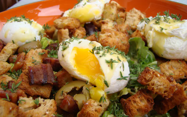 Close-up of a Salade Lyonnaise featuring poached eggs, crispy bacon, croutons, and greens, captured in HD as a vibrant lunch meal desktop wallpaper.