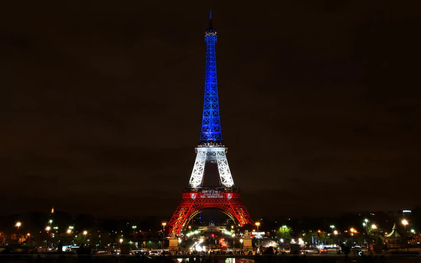 The Eiffel Tower illuminated in blue, white, and red lights against the night sky in Paris, France. This high-definition desktop wallpaper showcases the iconic structure in striking colors.