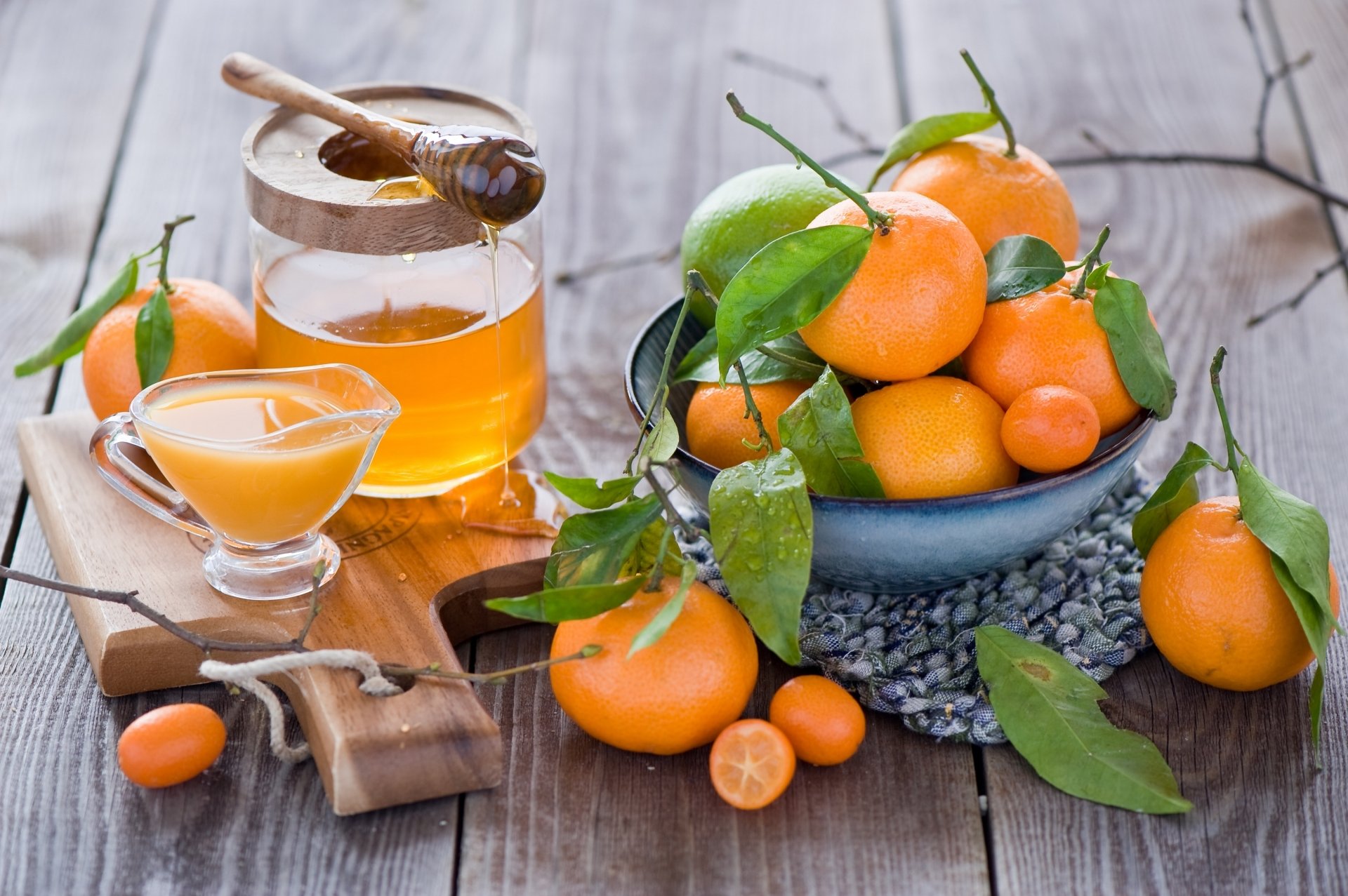 Still life HD desktop wallpaper featuring fresh mandarins with leaves, a jar of honey with a dipper, and a glass of juice on a rustic wooden table.