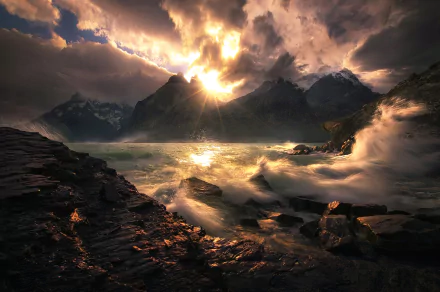 HD PC desktop wallpaper and background: sunbeams pierce storm clouds above jagged mountains while waves crash along a rocky coastline in a dramatic natural landscape.