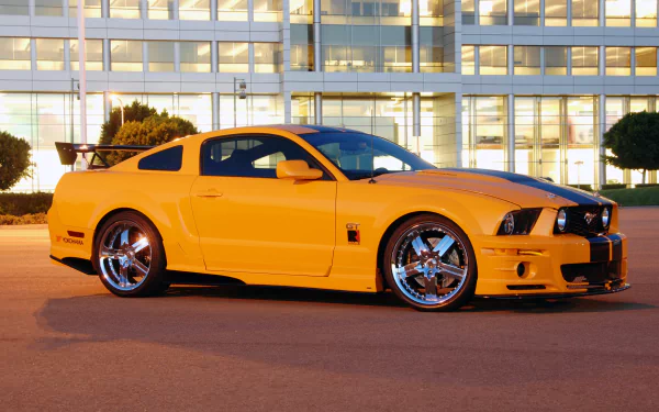 Yellow Ford Mustang Shelby muscle car parked in front of a modern glass building, captured in 4K Ultra HD for a desktop wallpaper background.