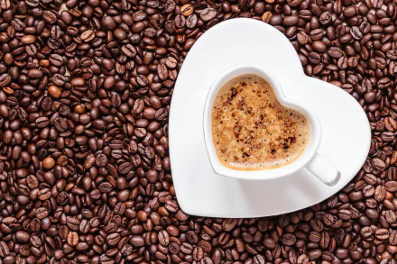 A heart-shaped cup of coffee rests on a white saucer, surrounded by a rich bed of coffee beans, creating an inviting 4K Ultra HD backdrop.