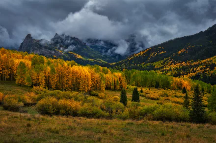 HD desktop wallpaper showcasing a dramatic fall landscape with golden forests, cloudy skies, and rugged mountains in Colorado, USA.