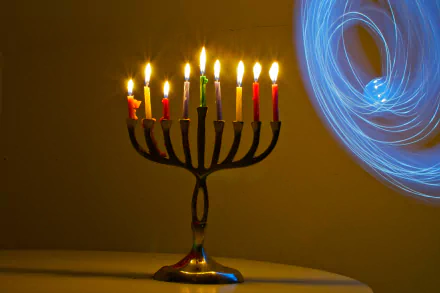 HD desktop wallpaper featuring a brightly lit Hanukkah menorah with nine colorful candles against a warm background and swirling blue light effects.