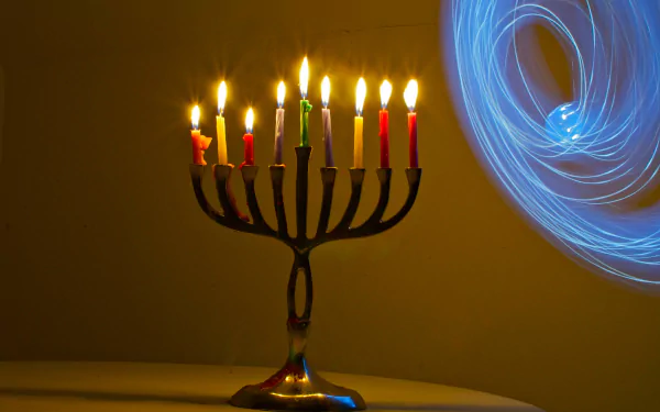 HD desktop wallpaper featuring a brightly lit Hanukkah menorah with nine colorful candles against a warm background and swirling blue light effects.
