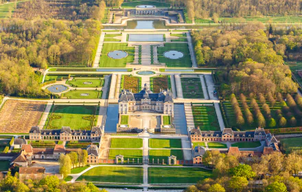 Aerial view of the man-made Vaux-le-Vicomte castle and park in Melun, France, showcasing intricate gardens and expansive grounds in HD detail.