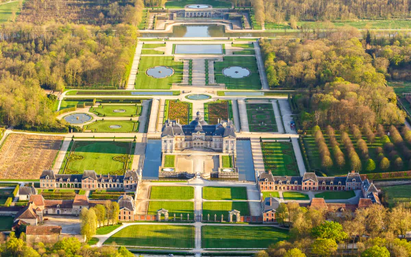 Aerial view of the man-made Vaux-le-Vicomte castle and park in Melun, France, showcasing intricate gardens and expansive grounds in HD detail.