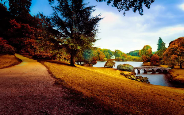 A vibrant park scene with a winding path, lush trees, and a serene lake, enhanced by autumn colors. Captured in stunning 4K Ultra HD for a striking desktop wallpaper.