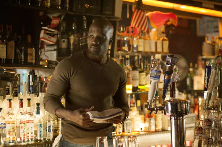 Mike Colter as Luke Cage stands behind a bar in a dimly lit scene from the TV show Jessica Jones, captured in 4K Ultra HD quality.