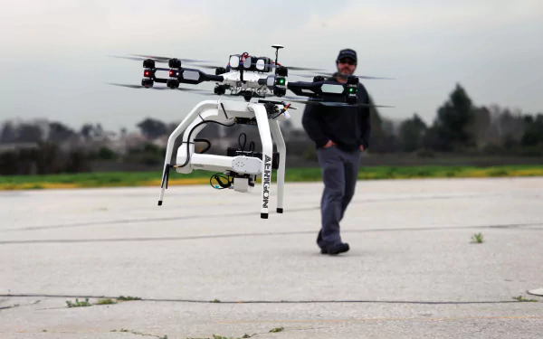 A man stands on a pavement as a drone hovers nearby. The image captures the advanced technology in action, showcasing a high-quality 4K Ultra HD background.