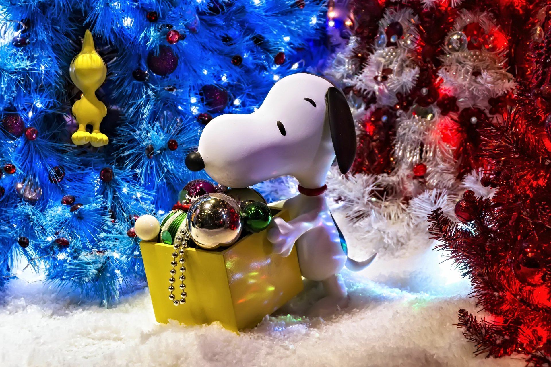 Snoopy surrounded by colorful Christmas ornaments amidst vibrant holiday decorations, set against a backdrop of festive trees, creating a cheerful holiday scene.