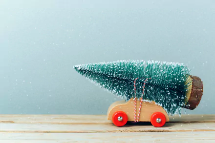 A wooden toy car carries a lush Christmas tree, evoking a festive holiday spirit amid gentle snowfall. This HD desktop wallpaper captures the essence of Christmas cheer.
