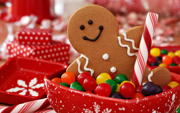8K Ultra HD holiday wallpaper featuring a smiling gingerbread cookie sitting in a festive red bowl filled with colorful candy and a striped candy cane.