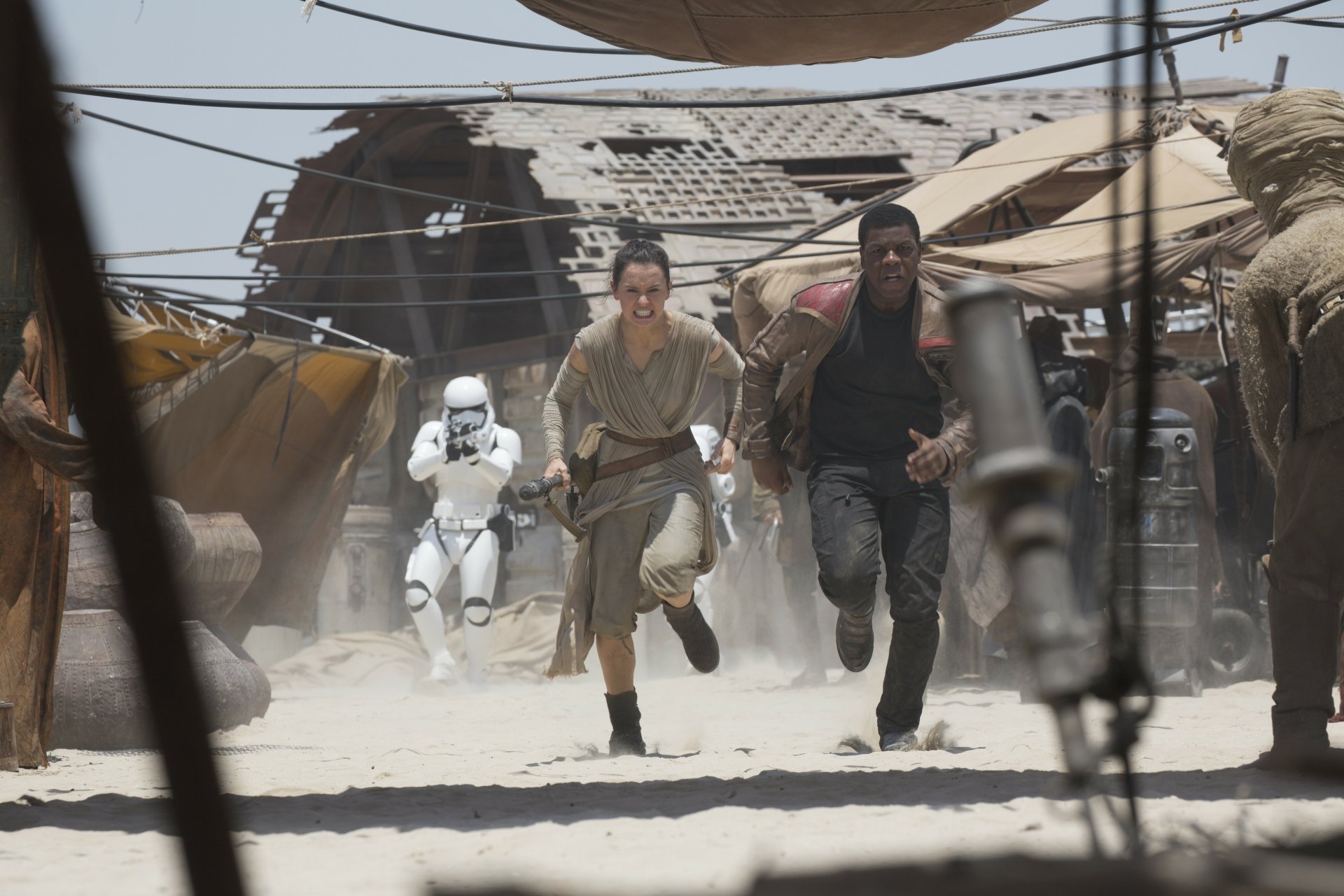 Finn (John Boyega) and Rey (Daisy Ridley) run from a stormtrooper in a desert scene from Star Wars Episode VII: The Force Awakens, shown in 4K Ultra HD.