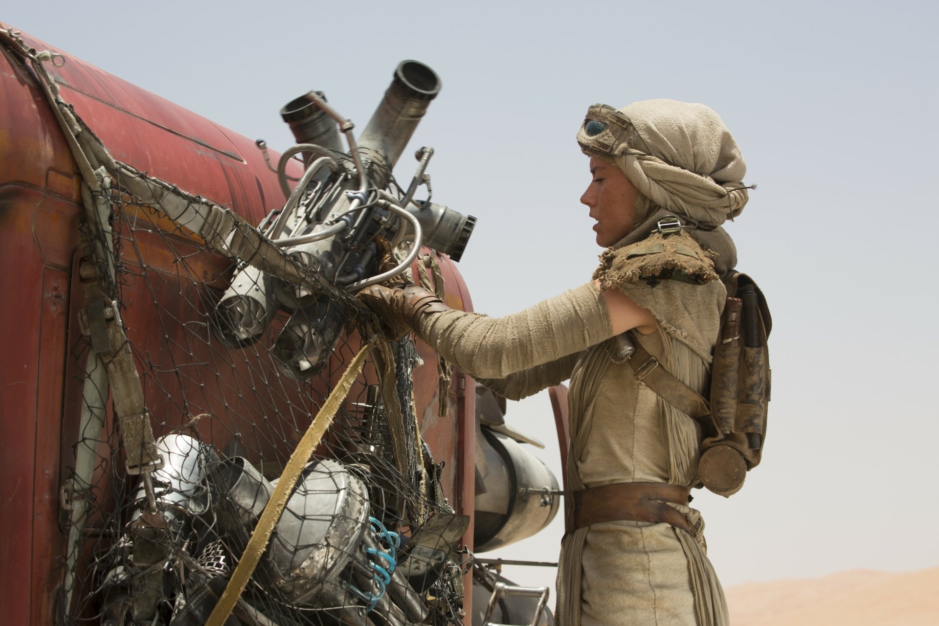 In this stunning 4K Ultra HD wallpaper from Star Wars: Episode VII - The Force Awakens, Daisy Ridley portrays Rey, a scavenger in a desert landscape, examining a heap of scrap metal.
