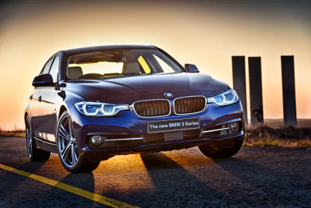 HD desktop wallpaper showcasing a sleek blue BMW 3 Series car illuminated by warm sunset lighting on an open road.