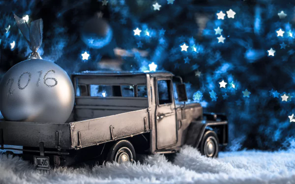 A vintage toy car carries a silver ball ornament engraved with 2016 against a backdrop of blue star-shaped Christmas lights in this 4K Ultra HD holiday wallpaper.