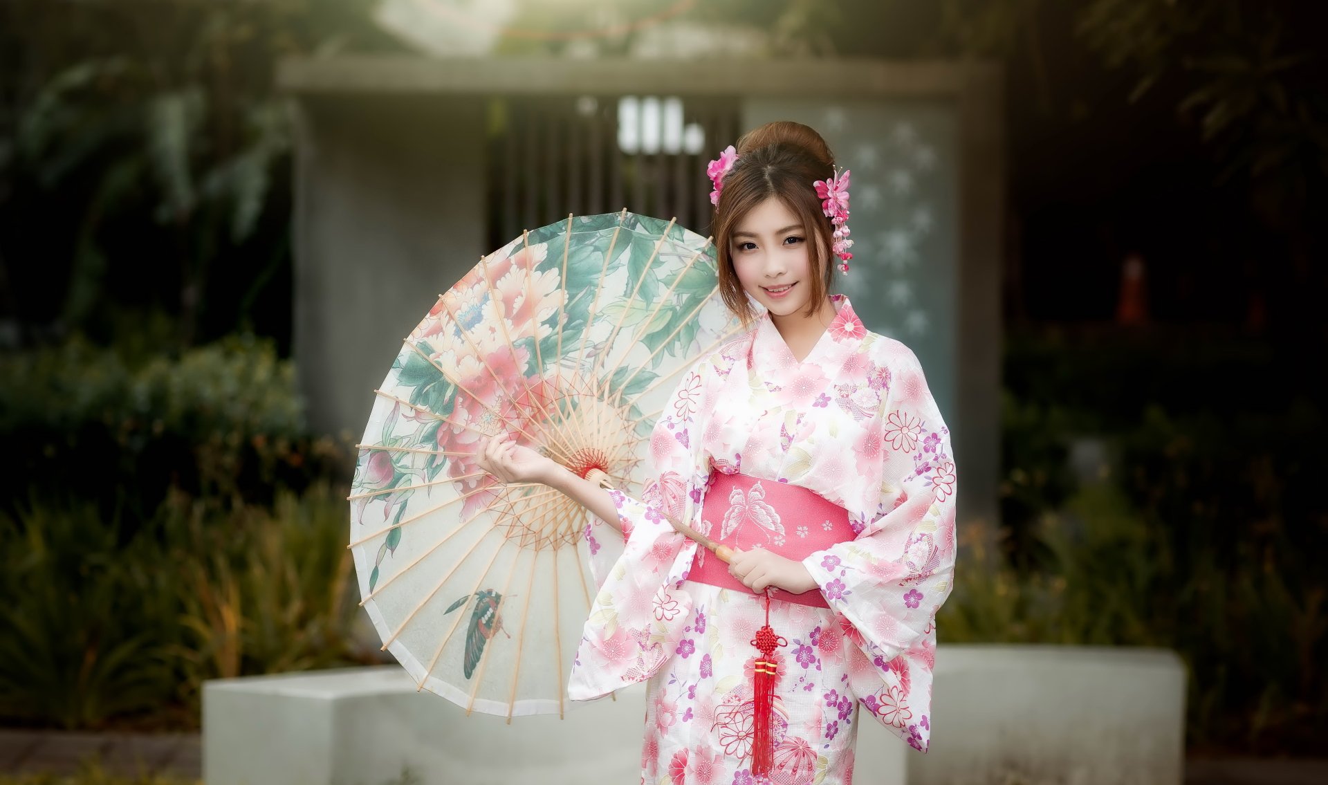 An Asian woman in a kimono holds a floral umbrella, with a background showcasing depth of field. The image features a serene garden setting, highlighted through HD wallpaper quality.