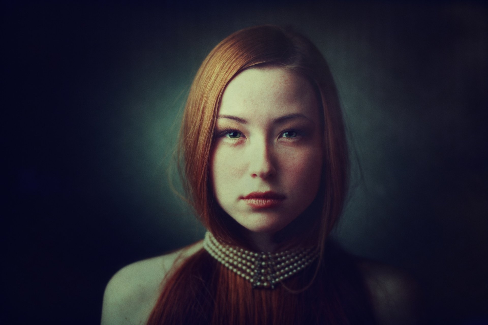 HD desktop wallpaper of a redhead woman with striking green eyes, straight hair, and a pearl necklace, captured in a poised and elegant model portrait.