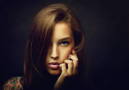 Close-up of a brunette woman with striking blue eyes and a contemplative expression, captured in HD quality against a dark background.