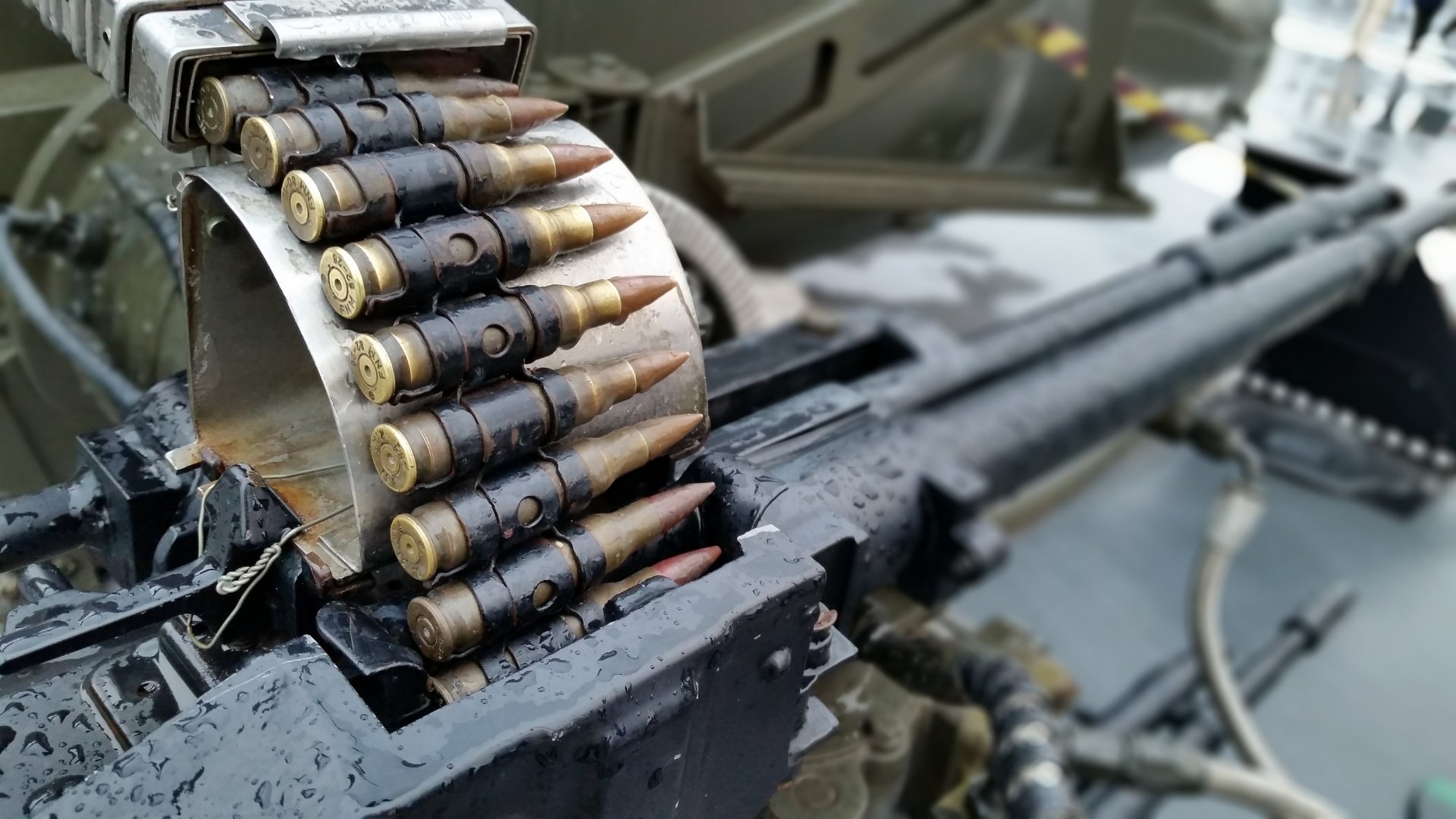 Close-up of a machine gun's ammunition belt, featuring bullets in a metallic drum. This HD desktop wallpaper showcases intricate details of man-made weaponry.