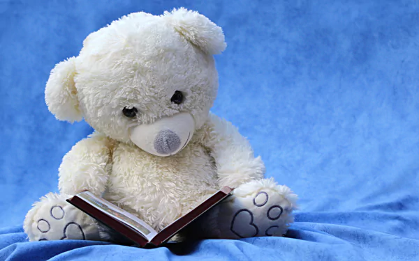 A plush teddy bear is sitting against a blue backdrop, holding a book open on its lap.