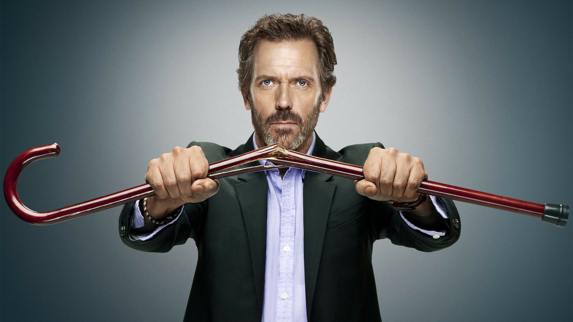 HD PC desktop wallpaper of a stern TV-show doctor in a suit gripping a bent red crowbar toward the viewer against a gray backdrop, house-themed.