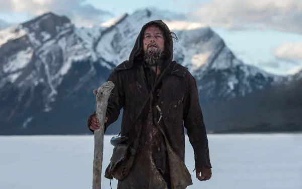Leonardo DiCaprio stands ruggedly against a dramatic mountainous backdrop in a scene from the movie The Revenant, showcasing the film's intense survival narrative.