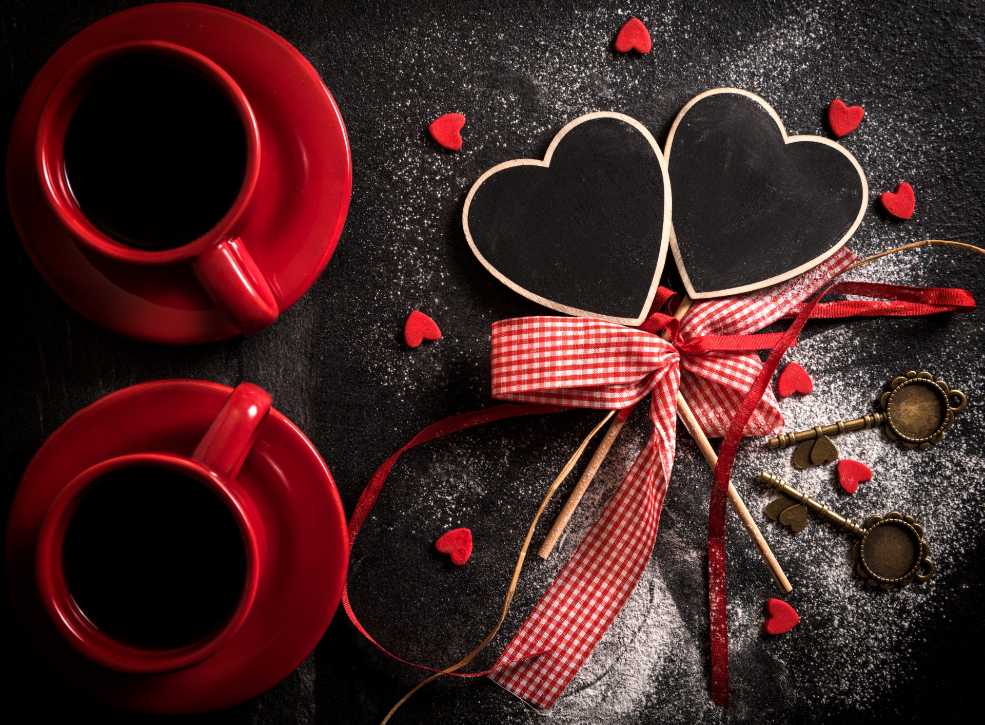 A romantic Valentine's Day scene featuring two red coffee cups, heart-shaped chalkboards, and small red hearts, all elegantly tied with a ribbon, set against a dark background.