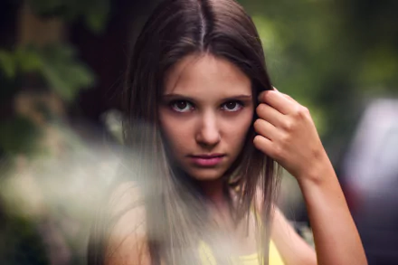 A brunette woman with brown eyes poses outdoors, highlighting her lipstick against a beautifully blurred bokeh background, creating a captivating HD wallpaper effect.