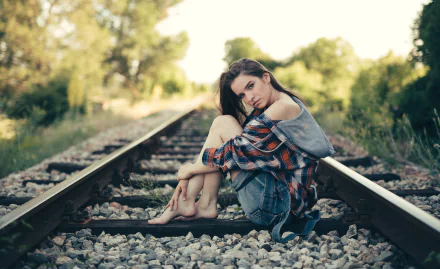 A brunette woman model sits barefoot on an outdoor railroad track with a soft bokeh background, captured in a moody HD PC desktop wallpaper and background.