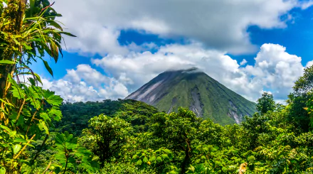 Lush green forest in El Salvador with a prominent volcano under a vibrant sky filled with clouds, captured in HD for a desktop wallpaper background.