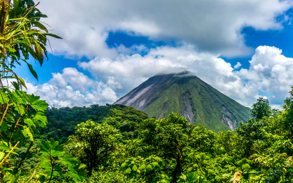 Lush green forest in El Salvador with a prominent volcano under a vibrant sky filled with clouds, captured in HD for a desktop wallpaper background.