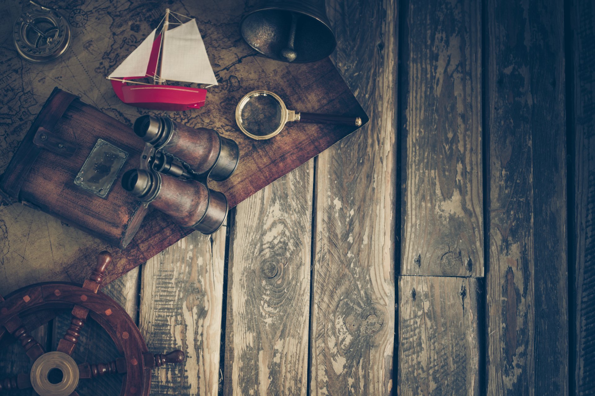 Vintage nautical items including a map, binoculars, a compass, and a toy sailboat arranged on rustic wooden planks, captured in 4K Ultra HD photography.