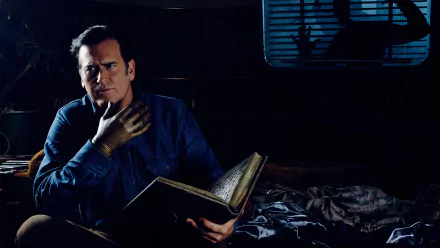 2K Quad HD PC desktop wallpaper from the TV show Ash vs. Evil Dead: brooding man in a dark room reads an ancient book, a metal hand glints beside a rumpled bed.