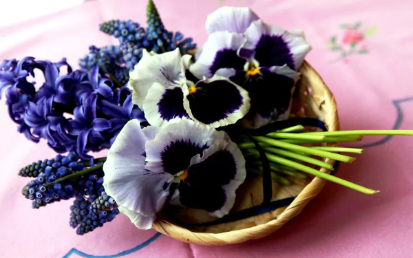 A vibrant 4K Ultra HD desktop wallpaper featuring a man-made arrangement of purple muscari, hyacinth, and pansy flowers in a woven basket on a pink floral cloth.