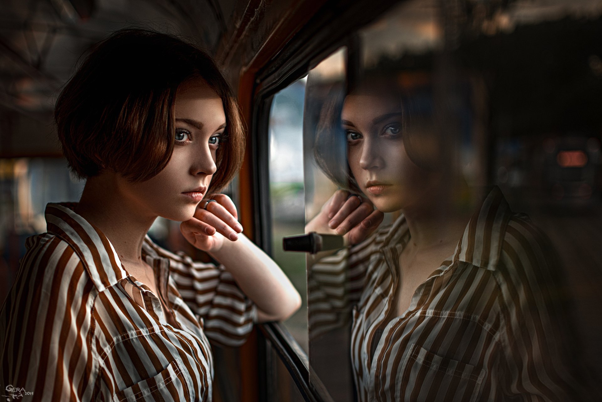 A stylish brunette woman with blue eyes gazes thoughtfully through a window, her reflection softly captured in this HD desktop wallpaper. Elegant and contemplative, it enhances any background.