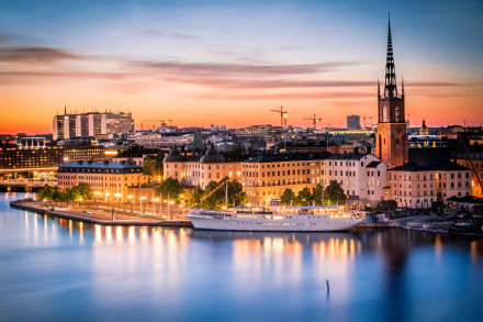 Dusk over Stockholm, Sweden showcasing city lights, historic houses, and a ship reflected in the calm water, creating a serene man-made urban landscape.