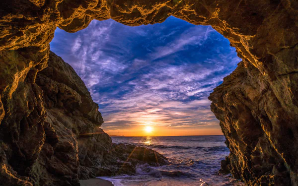 A stunning view from a cave in Malibu, California, showcasing a vibrant sunset over the ocean, with rich colors illuminating the sky and waves crashing on the beach.