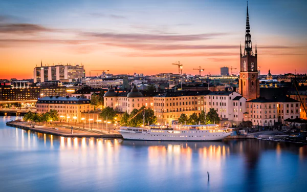 Dusk over Stockholm, Sweden showcasing city lights, historic houses, and a ship reflected in the calm water, creating a serene man-made urban landscape.