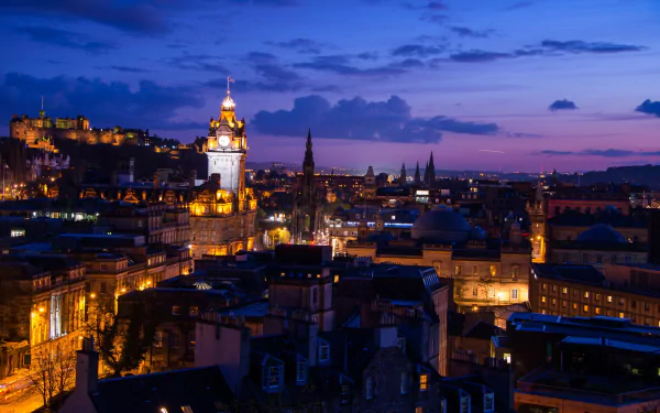 HD cityscape of Edinburgh, Scotland at night, showcasing illuminated historic buildings and a vibrant urban skyline under a deep blue sky.