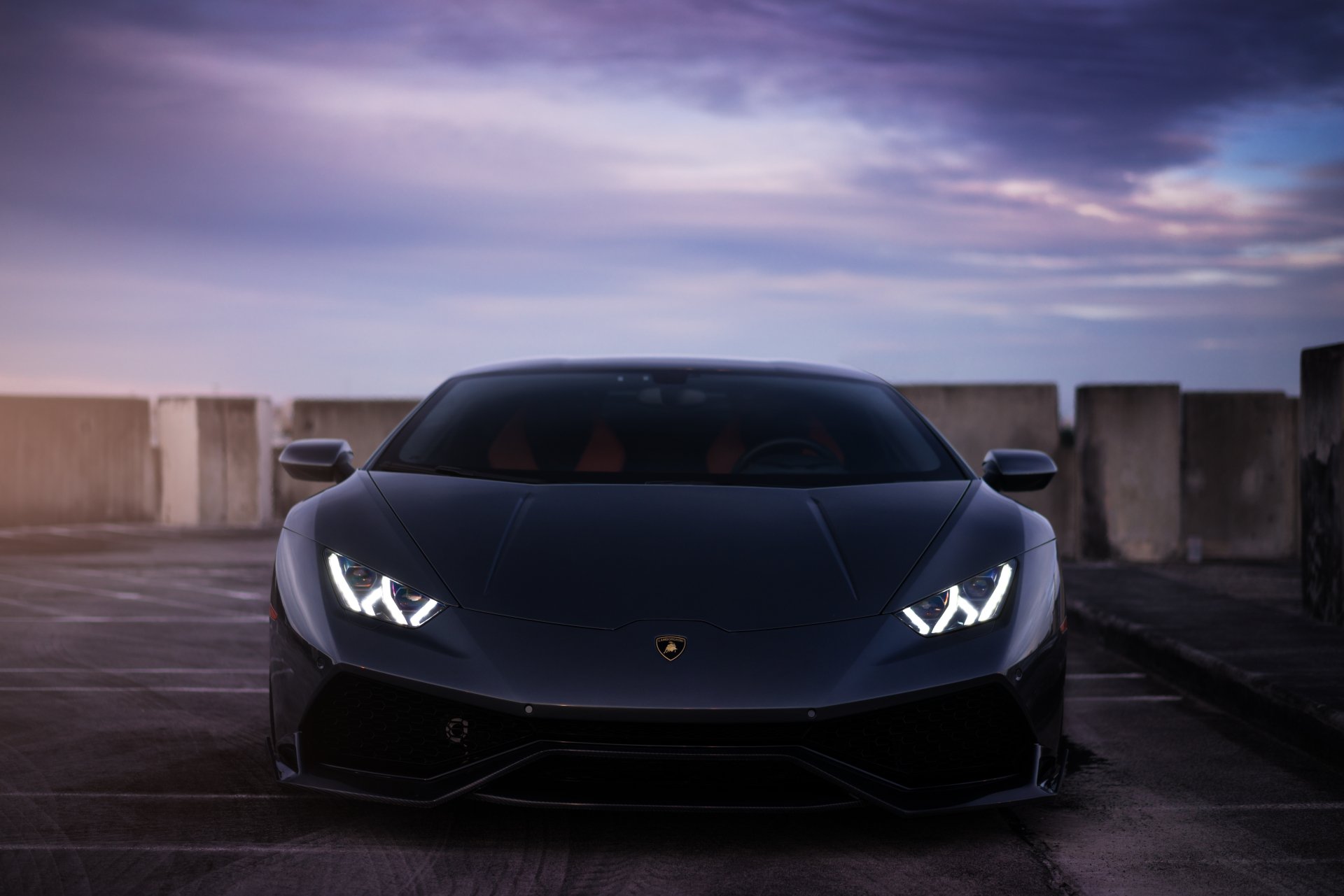 Front view of a matte black Lamborghini Huracan supercar, a performance car and vehicle with LED headlights on a rooftop at dusk — 5K Ultra HD PC desktop wallpaper background.