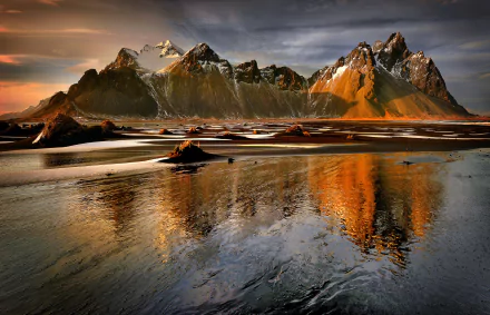 Stunning Vestrahorn Mountain reflects in calm waters, showcasing dramatic cliffs and a serene landscape under a moody sky. A breathtaking HD desktop wallpaper of nature’s beauty.