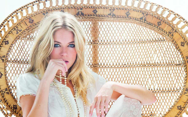 Blonde actress and model Sienna Miller with blue eyes, wearing a necklace, seated on an ornate chair in an HD desktop wallpaper background.