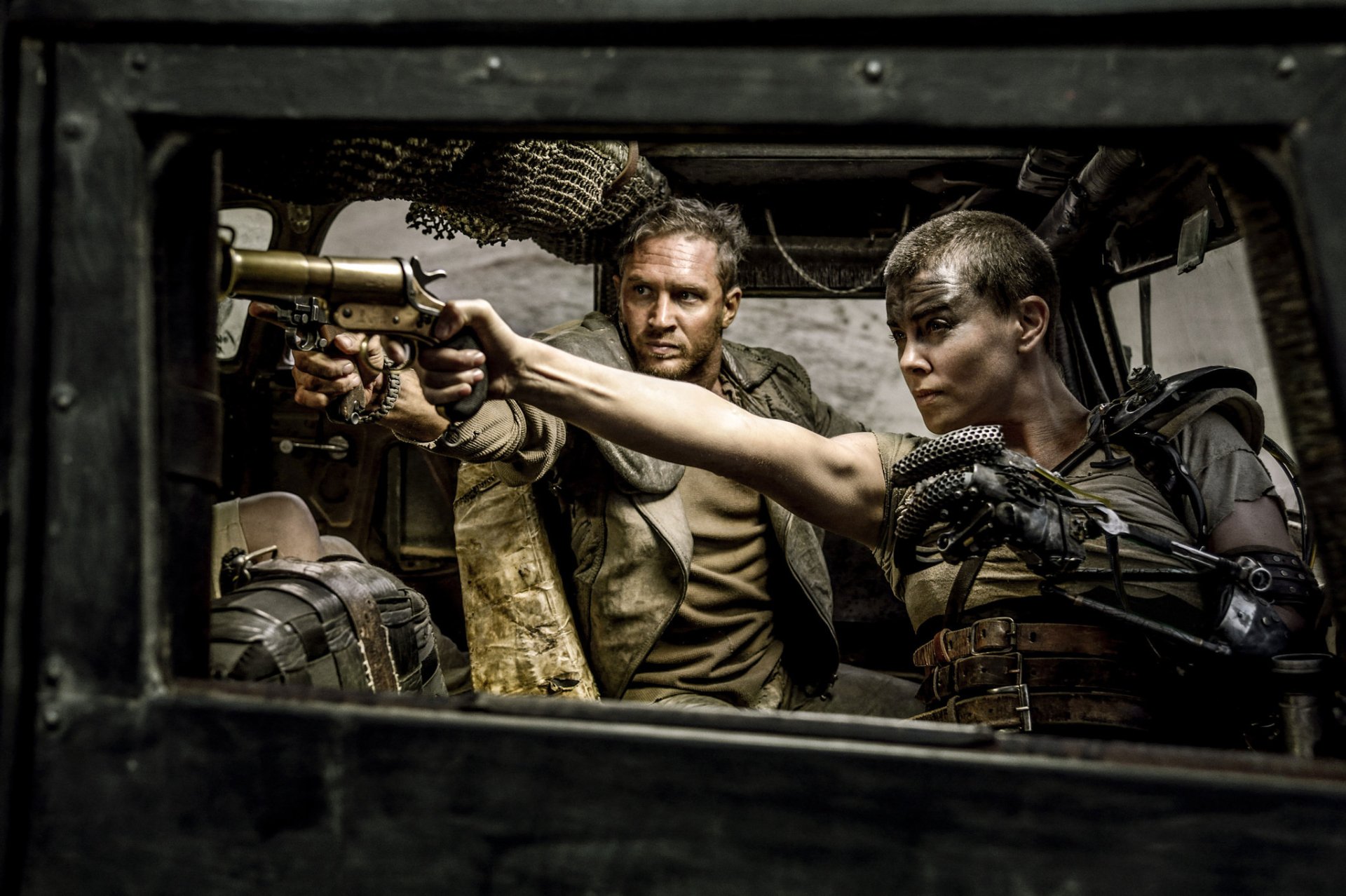 A thrilling scene from *Mad Max: Fury Road* featuring Imperator Furiosa (Charlize Theron) and Max (Tom Hardy) as they confront danger from within a vehicle.