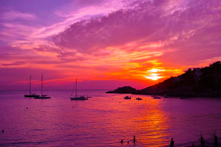 Vibrant 4K Ultra HD sunset over Ibiza, Spain, with orange and purple hues lighting the sky, silhouetted boats on the ocean, and a serene coastal landscape.