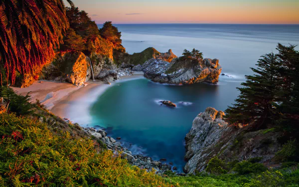 A serene beach scene in Big Sur, California, features a stunning coastline with a gentle waterfall cascading into the ocean, surrounded by lush greenery and tranquil waters.